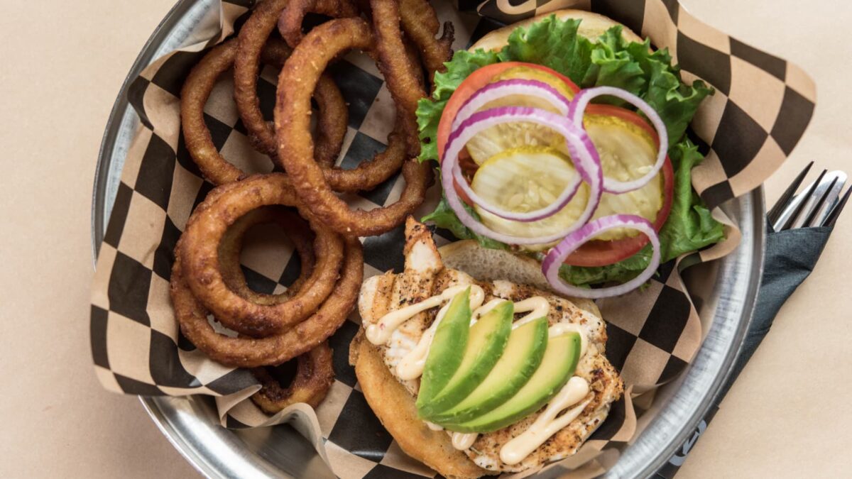 Grilled chicken sandwich with avocado, pickles, onions, and onion rings